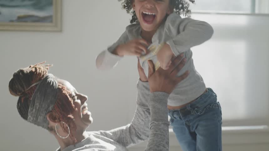 A mother lifts her son up in the air and laughs as they fall onto a bed