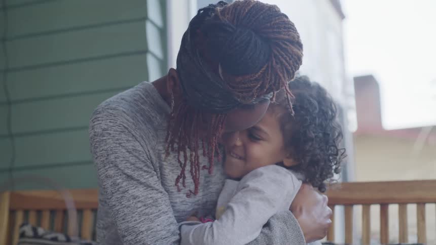 A woman smiles at a child on the bench next to her before embracing her