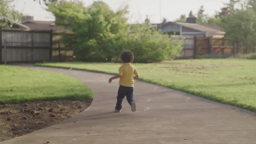 A little boy runs down a sidewalk chasing bubbles