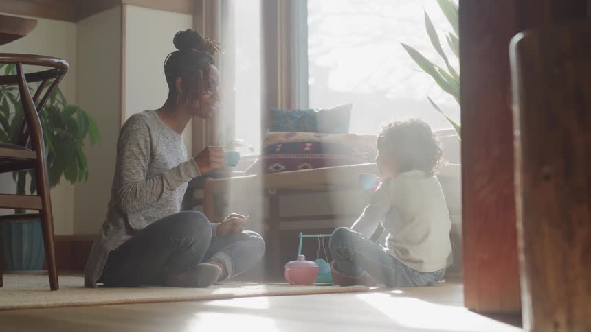 A woman and a child have a tea party on the floor of the living room