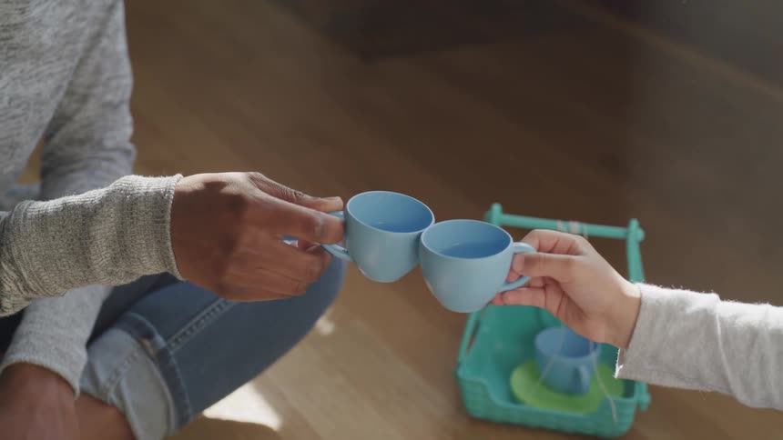 A little girl and a woman clink mugs together as they have a tea party