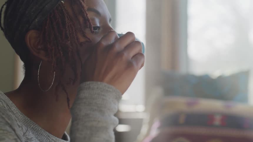 Black woman drinks from cup and smiles indoors during daylight