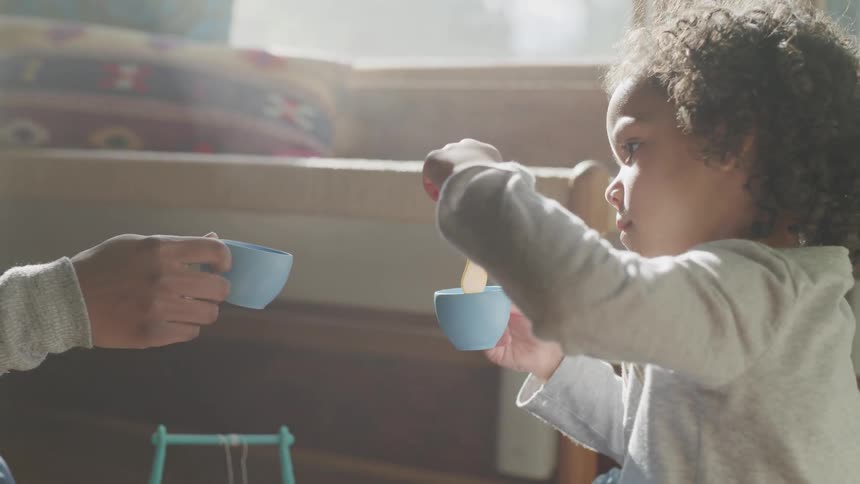 A young girl is hosting a tea party and using a play spoon to stir liquid in toy teacups