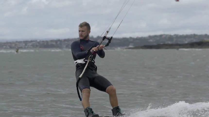 A man kite surfing in the foreground with several others kite surfing in the background on a cloudy day