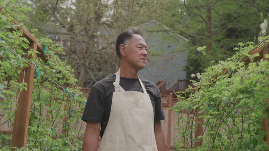 Asian man standing in between two vine plants
