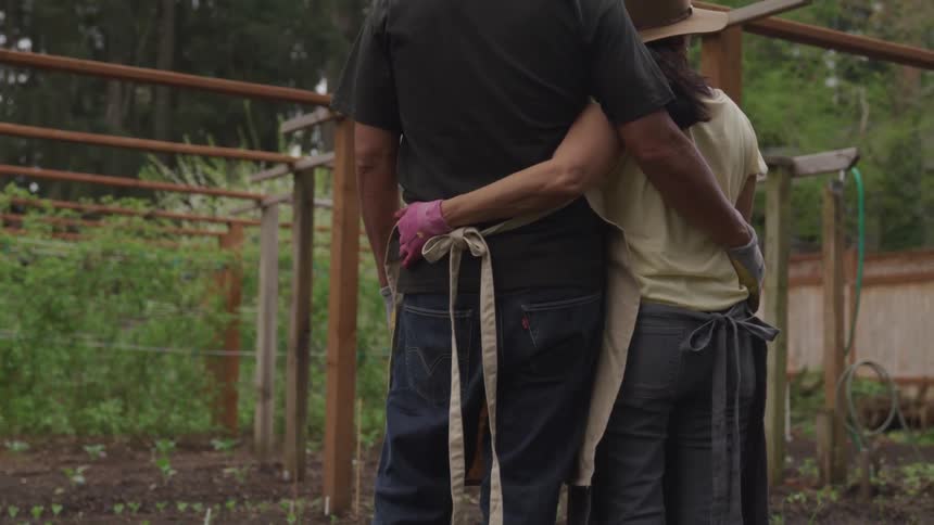 Two people hug near a garden
