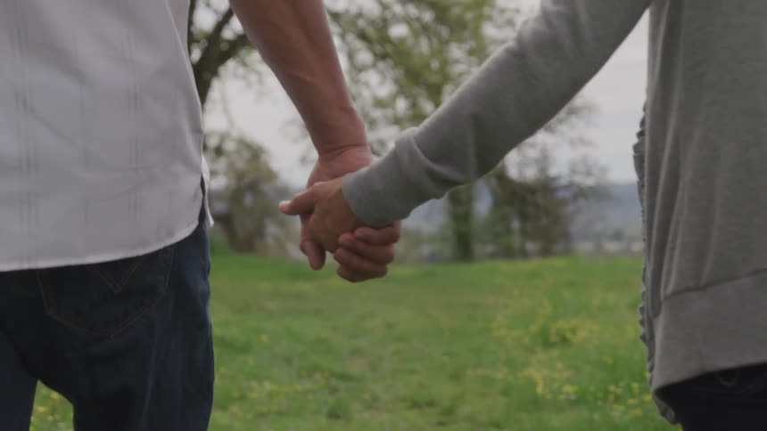 Man and woman hold hands and walk on the grass during daylight