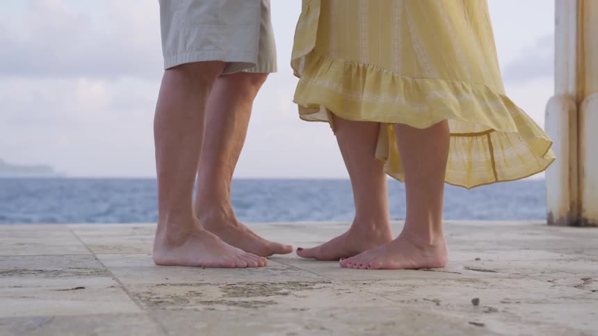 A barefoot man and woman standing on a concrete pathway next to the sea