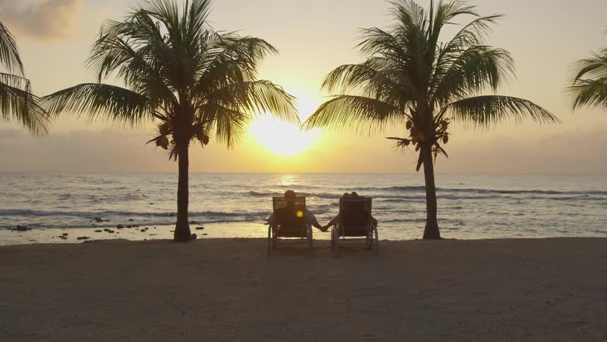 A couple holds hands while sitting on the beach
