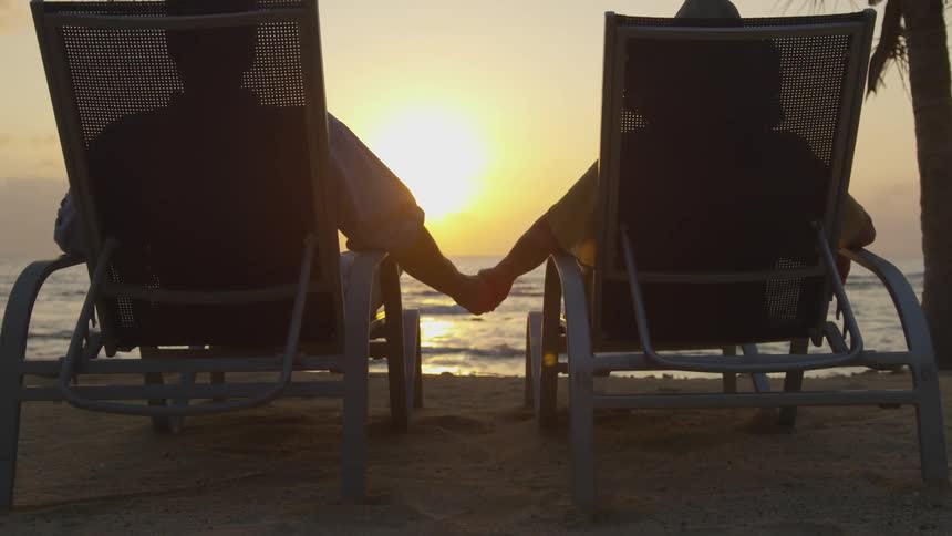 A couple sits on the beach holding hands