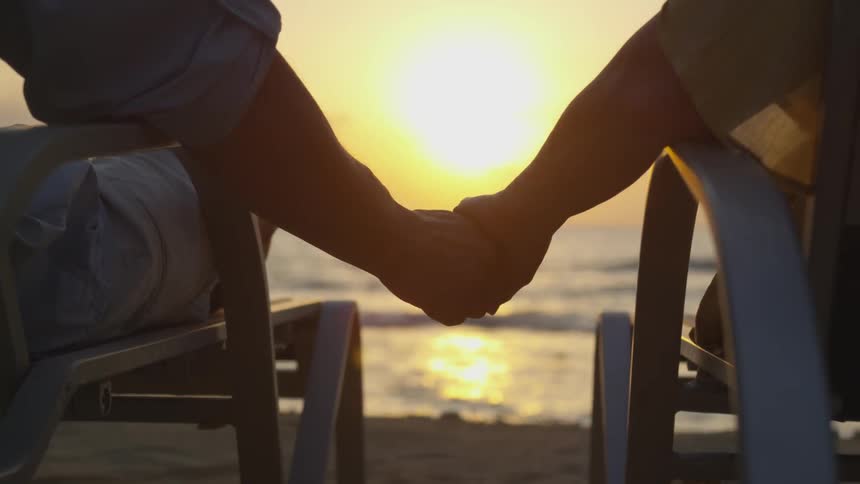 A couple hold hands while watching the sunset on the beach