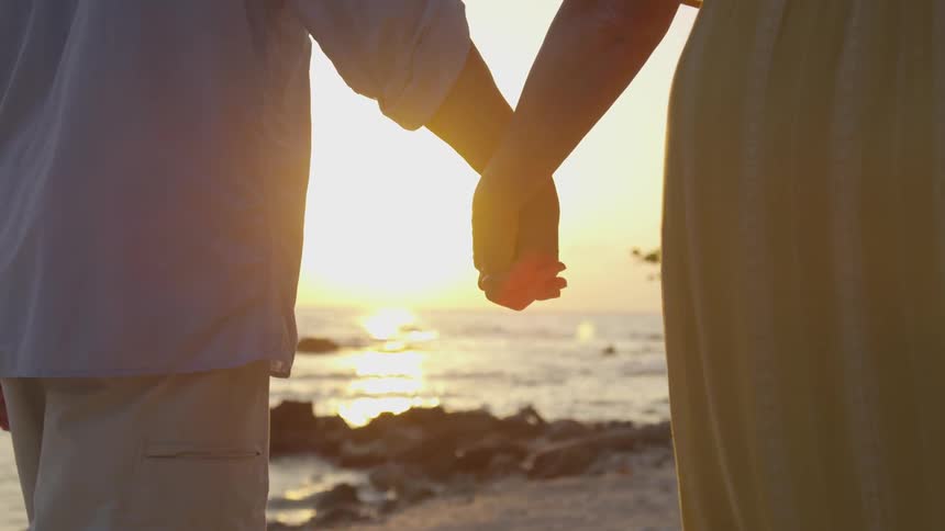A couple holds hands as they walk beside the coast line