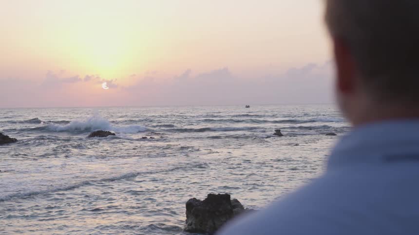 A man is looking out over the water at sunset
