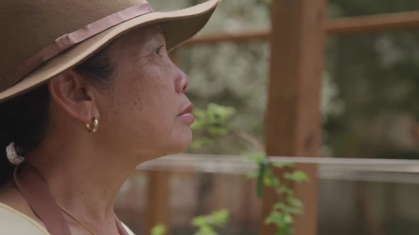 An older asian woman in a wide brimmed hat stares intensely at something in front of her