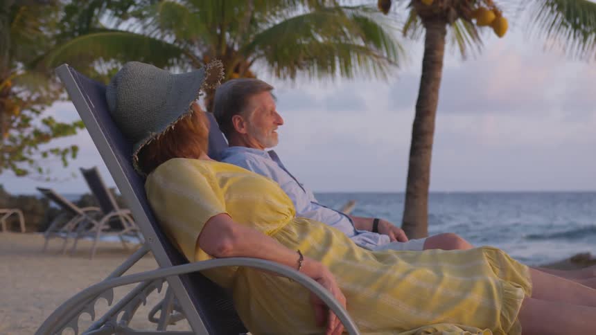 A man and a woman sitting on gray chairs on the beach