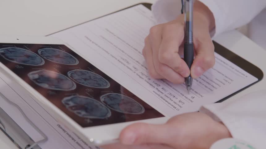 Doctor uses tablet and takes notes in the office during daylight