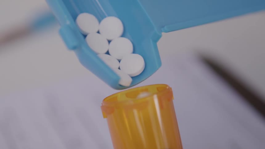 Pills are poured carefully into a pharmaceutical bottle from a tray