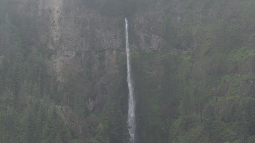 A long waterfall on a very steep mountain range covered in trees