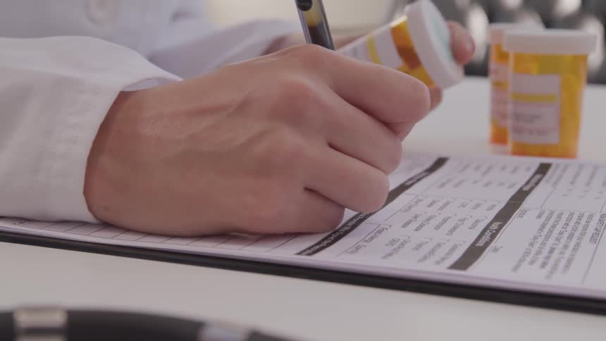 A person is holding a prescription bottle and writing on a piece of paper
