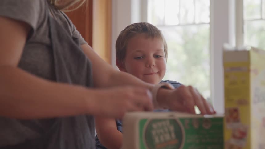A young boy smiles and watches as an adult woman cracks an egg into a mixing bowl in a kitchen