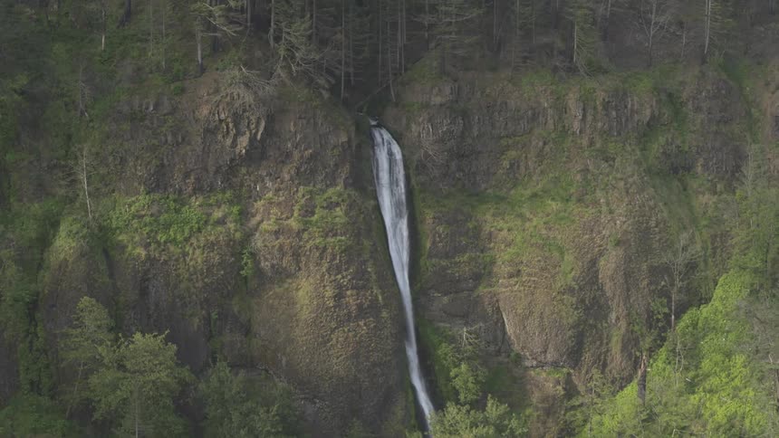 Aerial footage of a high up water fall between two rocky cliffs in a forest area