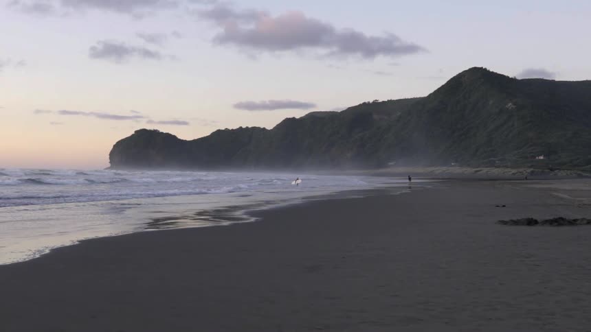Waves roll in next to a rocky mountain at sunset