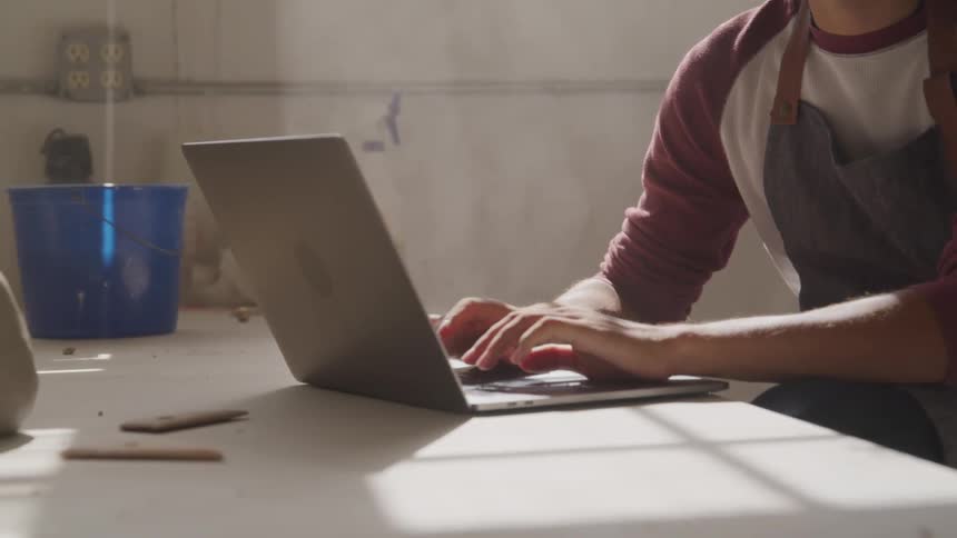 Man in apron typing in laptop on a desk