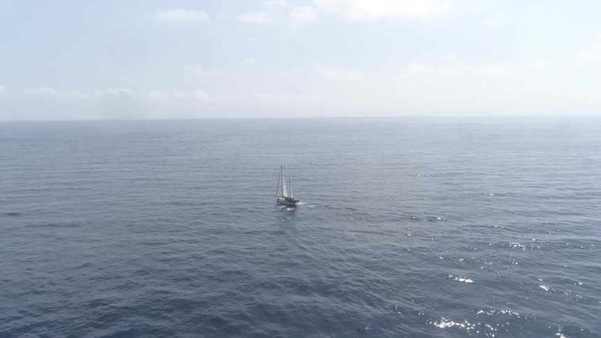 A sailboat in the ocean with the sky and clouds in the background