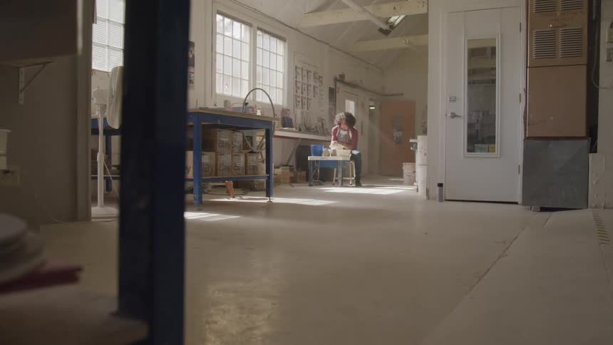 A man sits at a low table in a studio working with clay