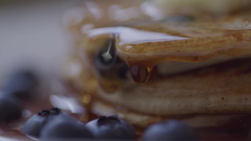 Syrup being poured over blueberry pancakes