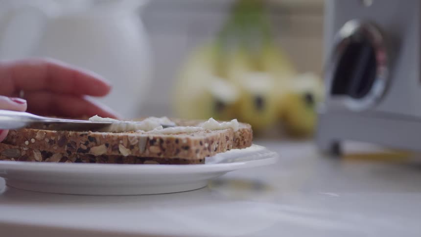 A woman spreads butter on a slice of bread on a plate