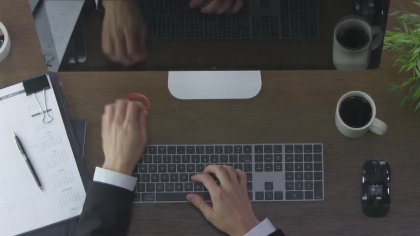 A man types on a computer keyboard and fidgets with a rubber band
