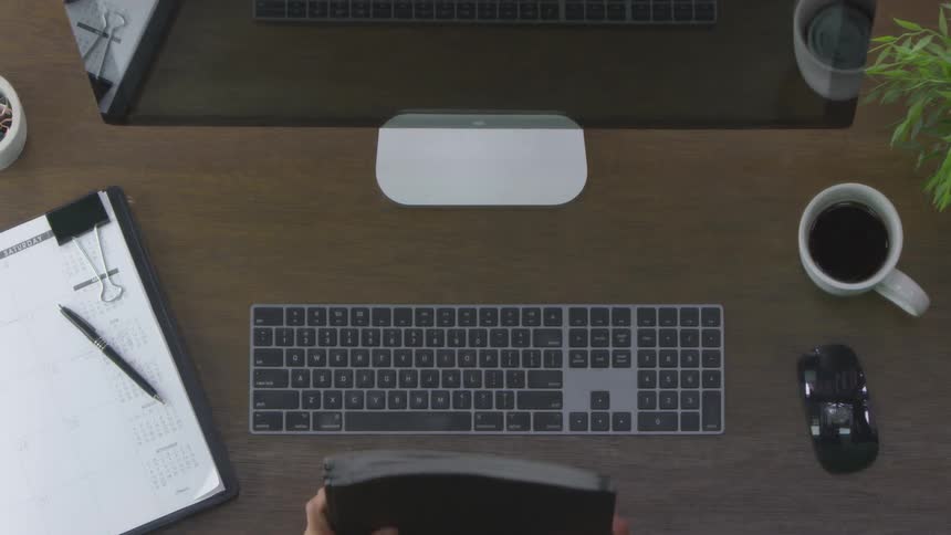 A person gathers the black folders on their desk moves them to the left and begins typing on their keyboard