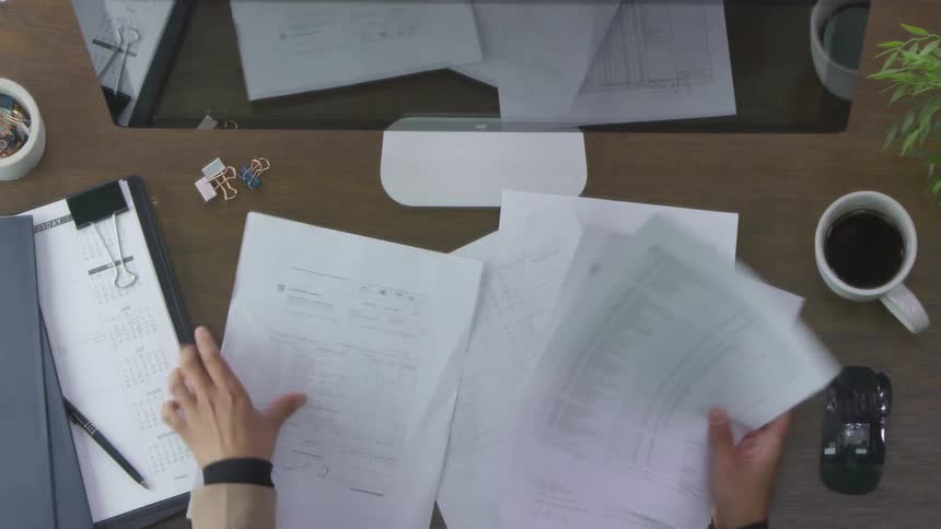 A person looks through papers on a desk then throws them in the air