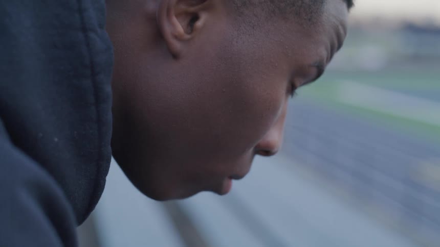 A black man contemplate on the bench near the field