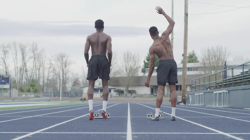 Two men stretch and jump on a running track