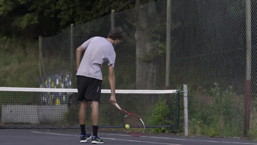 Male Tennis Player Serving Ball Outdoors on Court during Sunny Day Match.