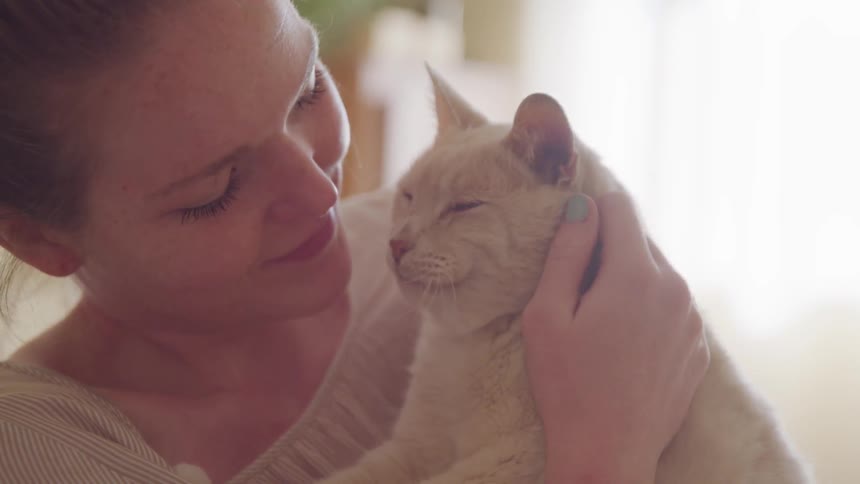 A woman holds and kisses her cat while indoors