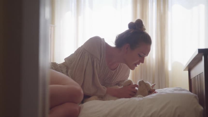 A woman sitting on a bed playing with a white cat