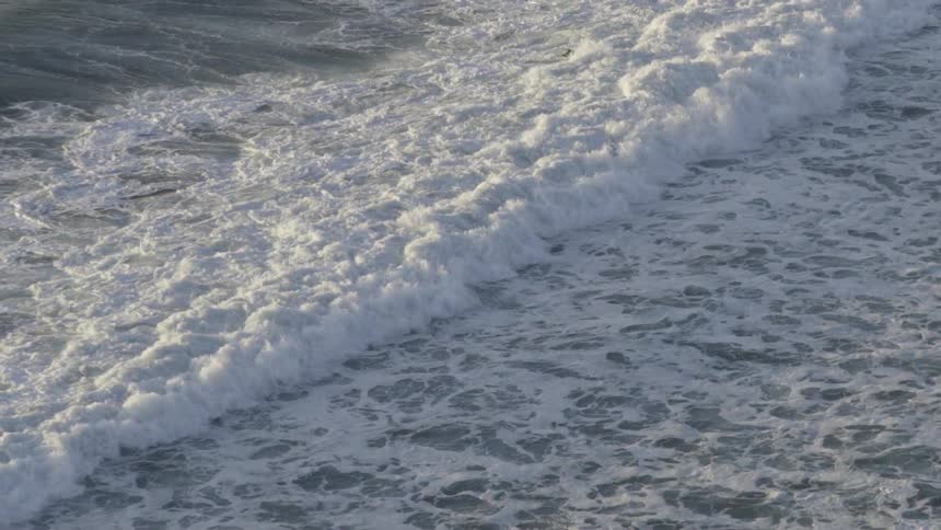 Strong ocean waves hit the sandy shoreline, creating mist and energy at the coast.