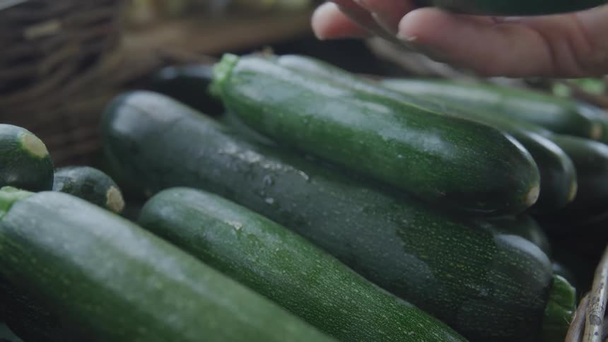 A person is picking up a zucchini