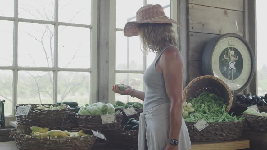 A woman in a vegetable market picking up a vegetable