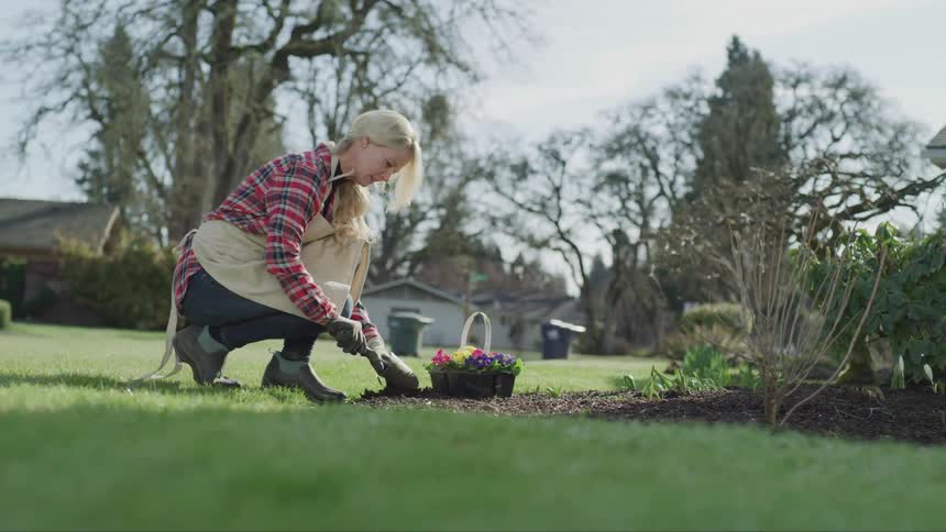 Woman works in a garden with a bucket of flowers nearby