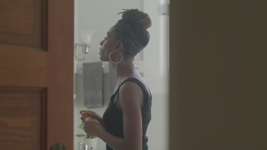 Black woman looks in the mirror and puts on makeup indoors during daylight