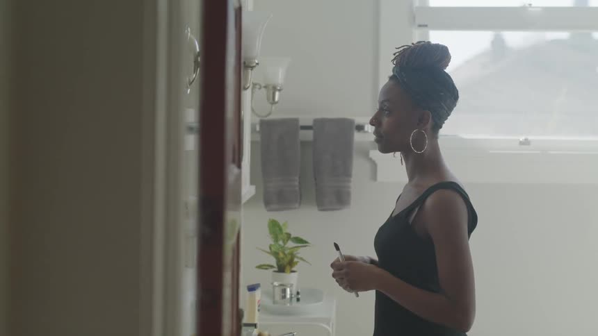 Black woman looks in the mirror and puts on makeup indoors during daylight