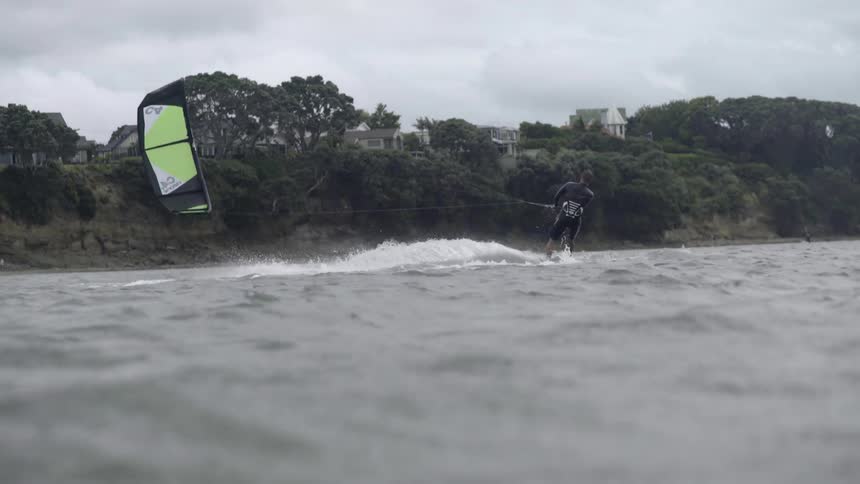 A man rides a sailboard across a calm water surface, wind-surfing in a peaceful setting.