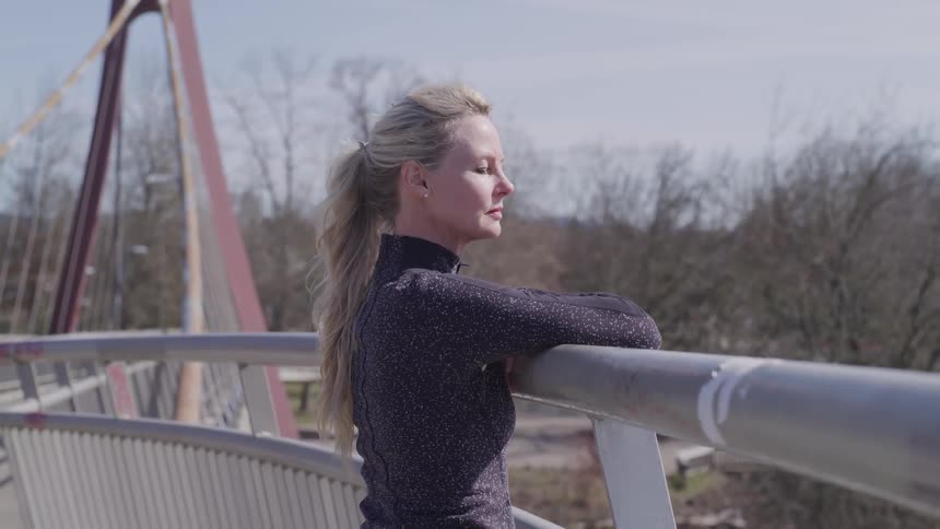 Woman leans on the railing of a bridge