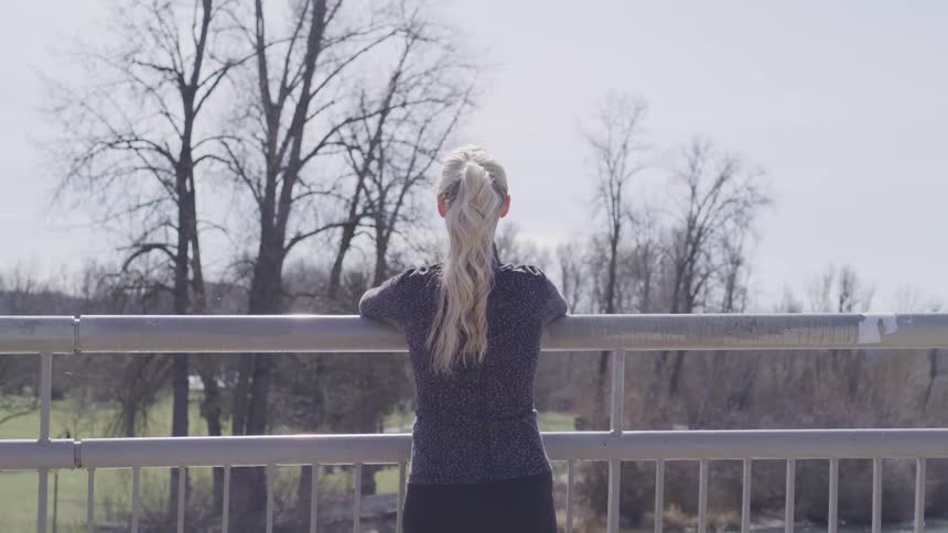 A woman stands on an overpass looking over a park