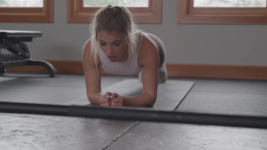 A woman in a sports vest and yoga pants works out in a bright room