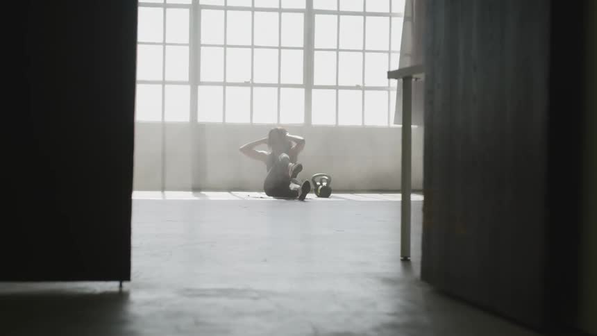 A woman indoors on the floor doing sit ups